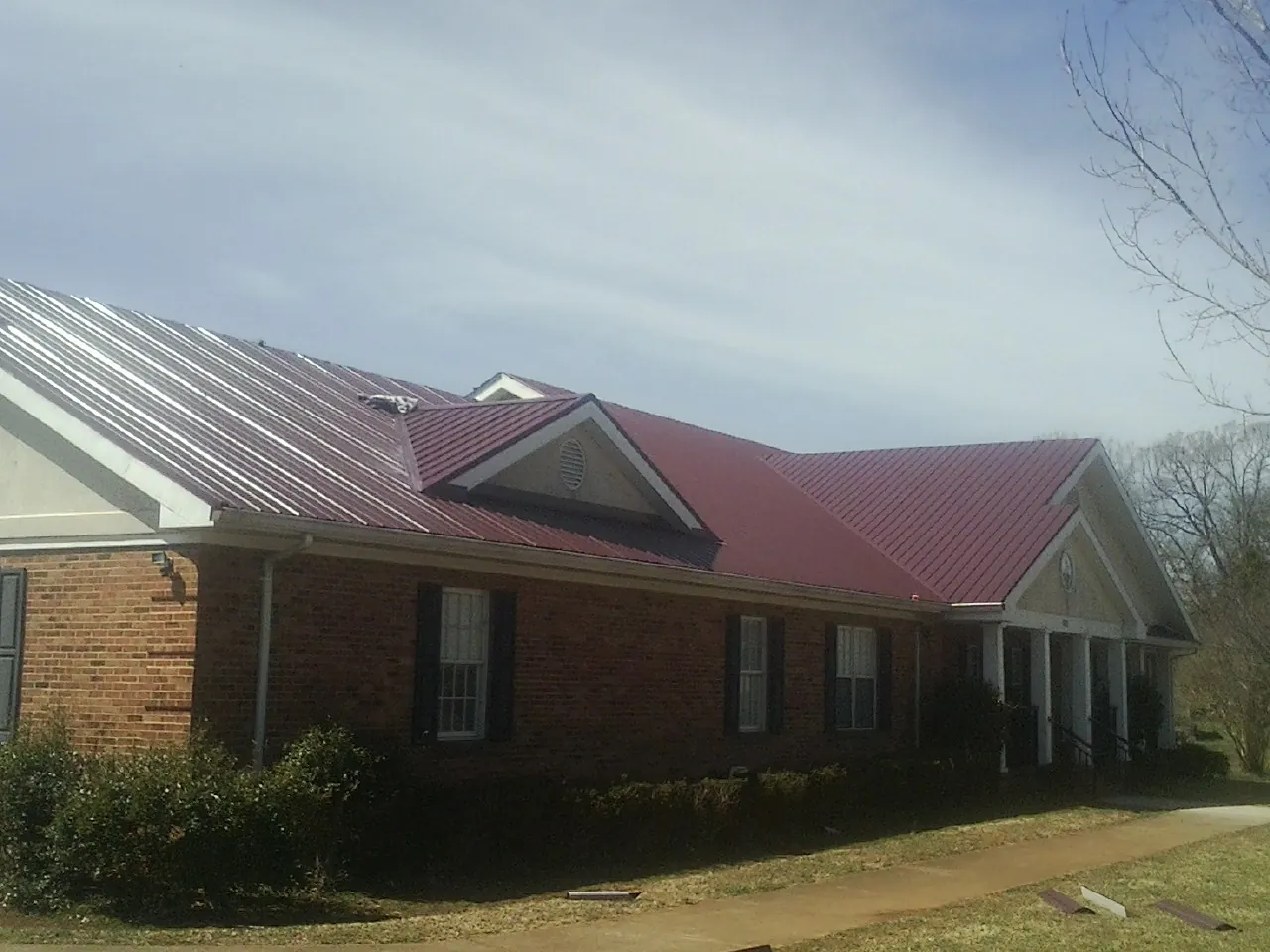 Red metal roof with gabled entries on a long brick building, from a Hail Damage Roof Repair job in Ridgefield Park