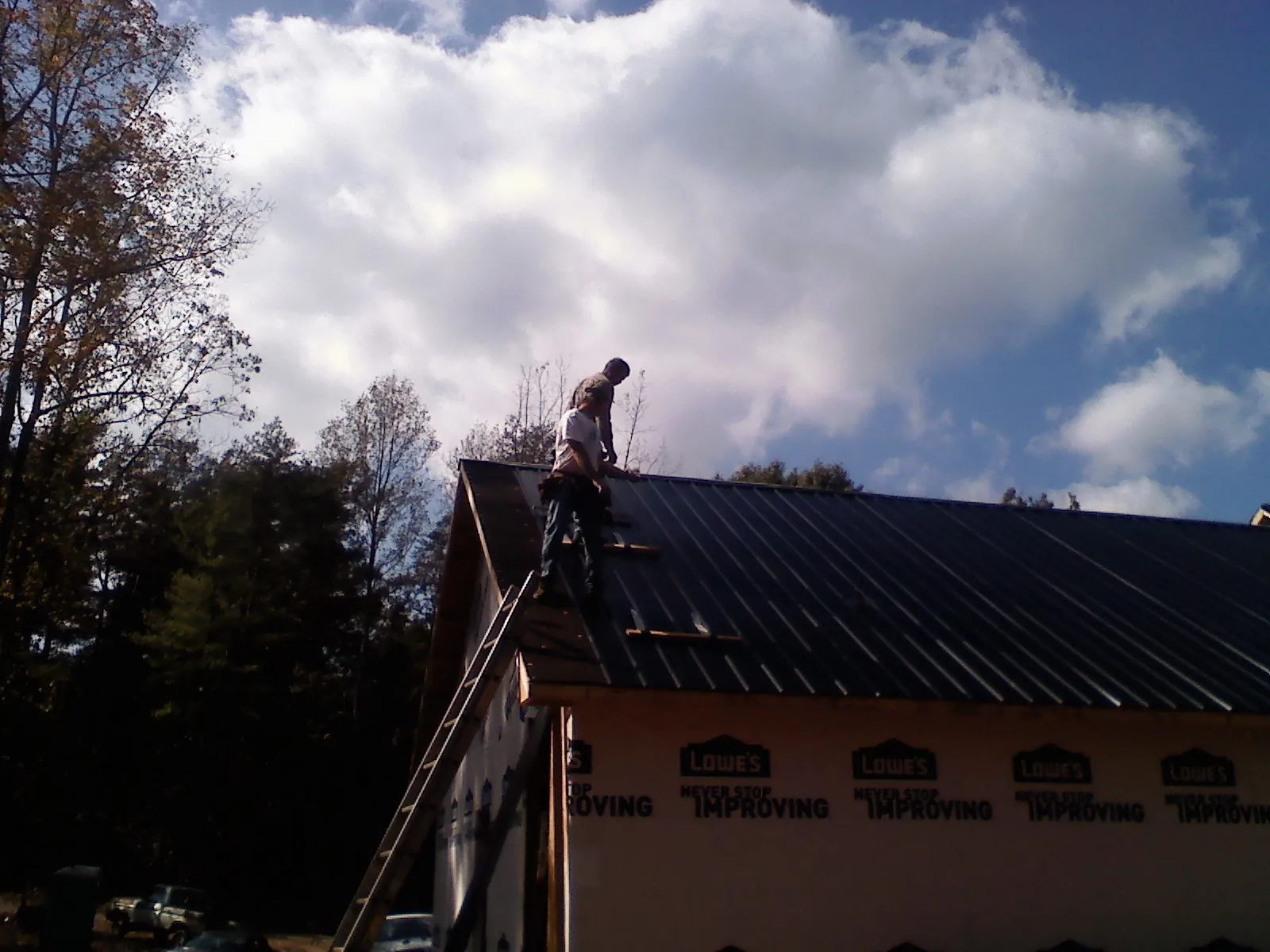 Roofer fastening dark metal panels high against a cloudy sky, from a Roof Inspection job in Ridgefield Park