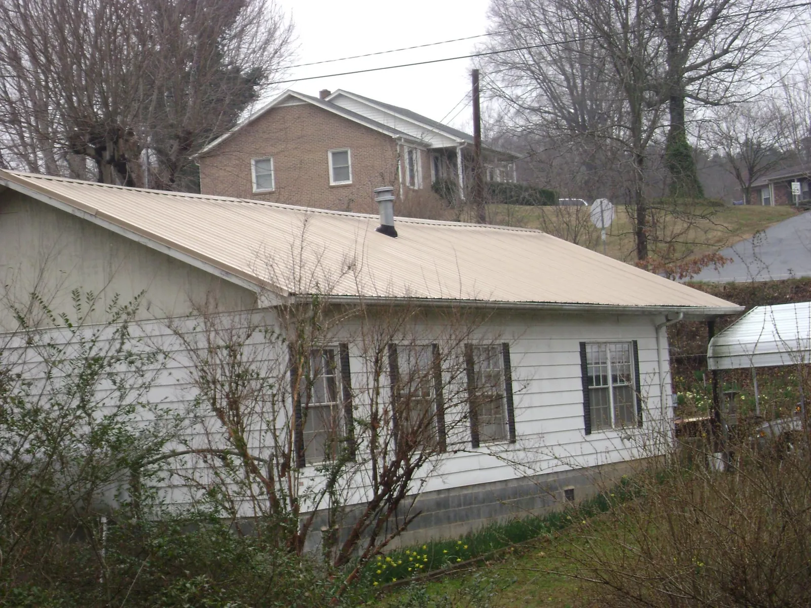 Tan metal roof on a white sided house set into a hillside — Commercial Roofing by Roofing Brothers in Ridgefield Park